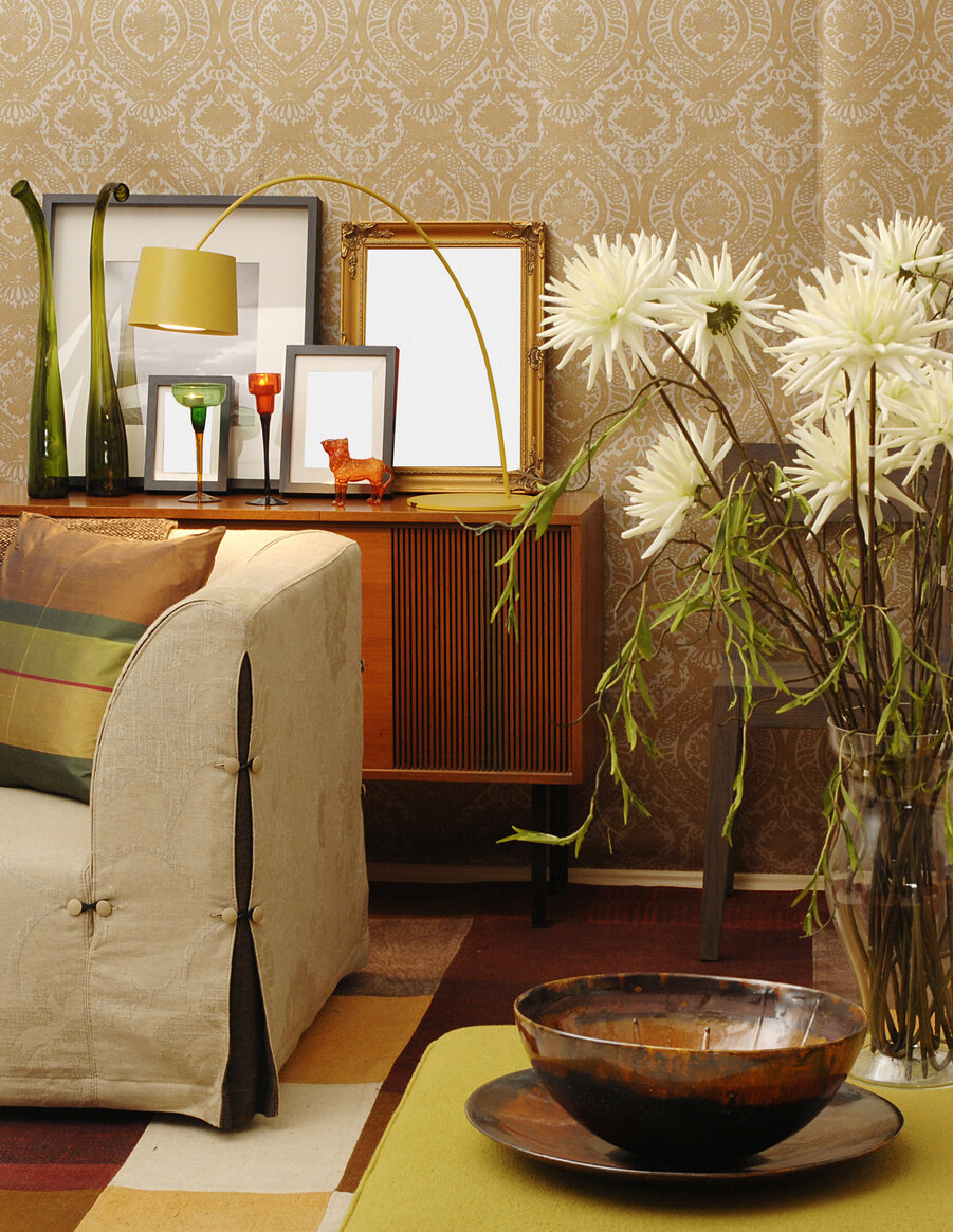 Tapete mit Muster, Sofa, Tisch mit Schale und Blumenvase, Kommode mit Bildern im Hintergrund